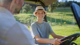 Young man in a straw hat drives a tractor as his father watches. | Pojoslaw | Dreamstime.com