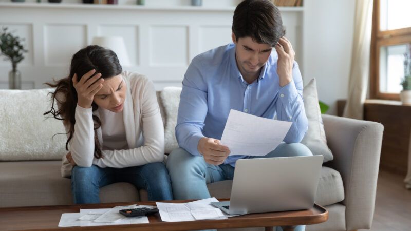 Man and woman sitting on couch and aghast at a bill. | Photo 184929007 © Fizkes | Dreamstime.com